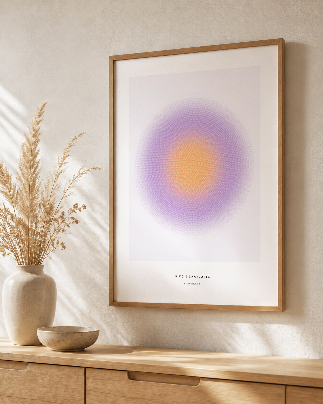 A light-oak framed print of a violet and amber radial artwork hanging above a wooden sideboard in soft daylight